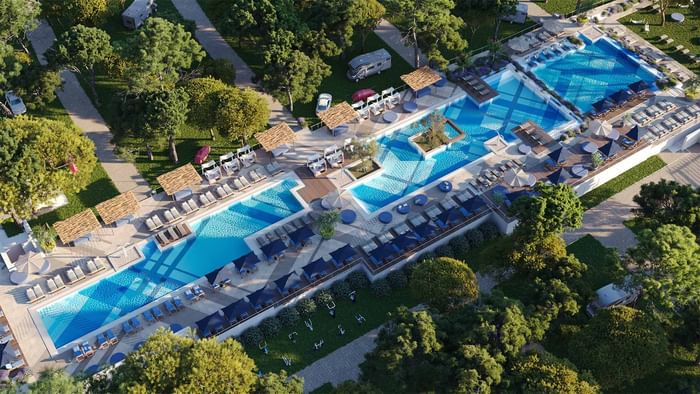 Vista aerea di un resort con tre piscine, lettini, ombrelloni e alberi circostanti.