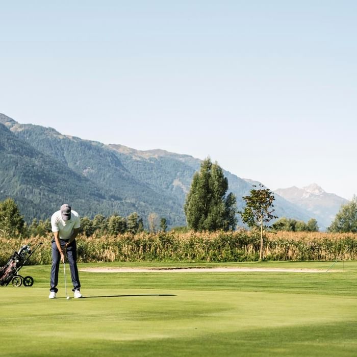 Golfer on a course with a mountain backdrop, preparing to putt near Falkensteiner Hotel and Spa Carinzia