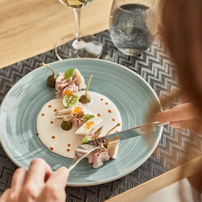 A person dining on a dish with a cream sauce, garnishes, and a wine glass at Falkensteiner Hotel and Spa Carinzia