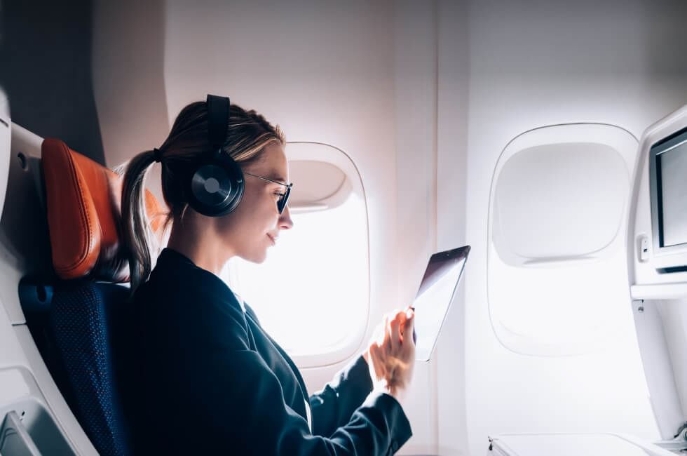 Una mujer en un avión trabajando en una tableta y usando auriculares