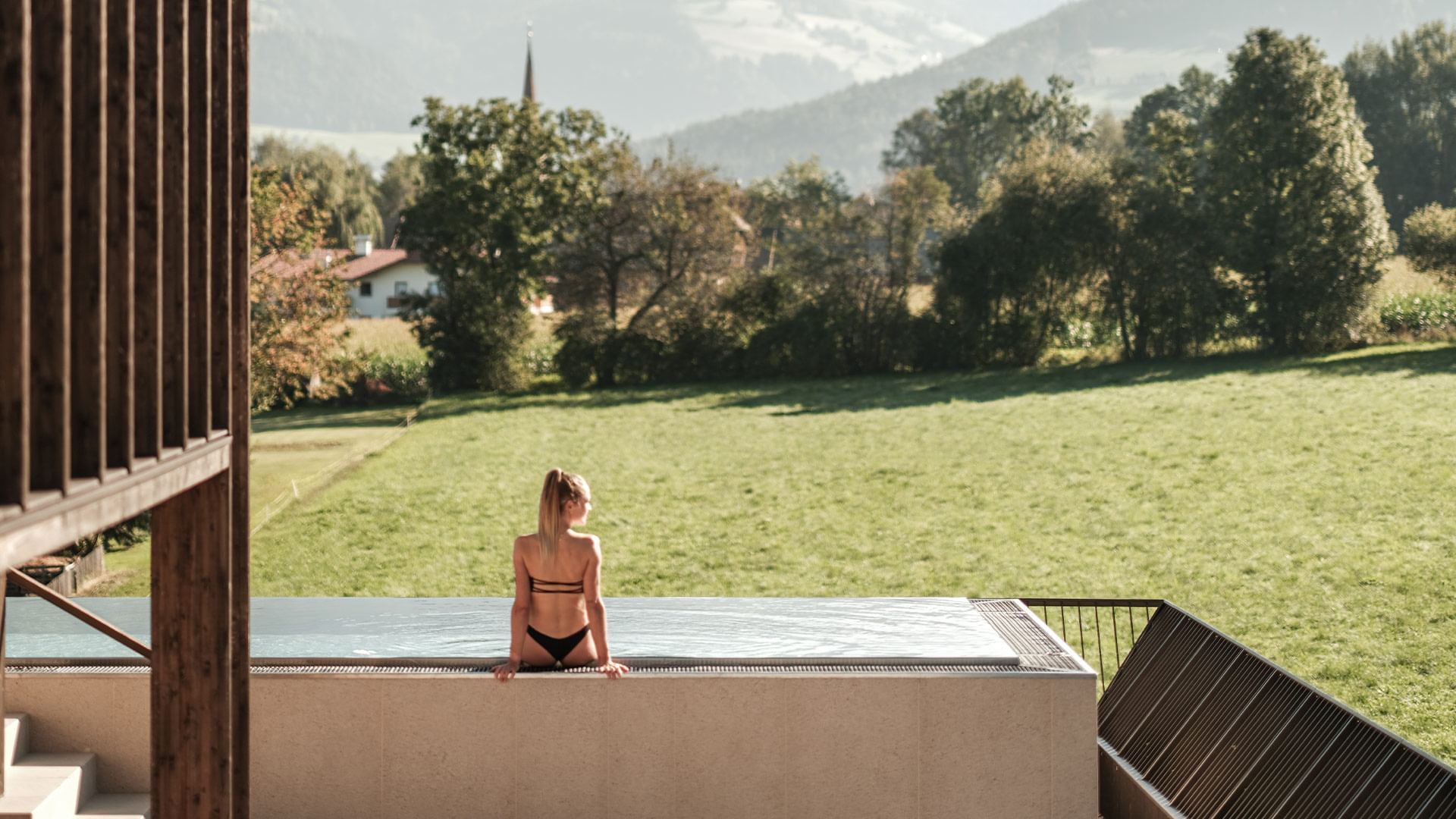 A lady sits by an outdoor pool enjoying a view at Falkensteiner Hotels & Residences