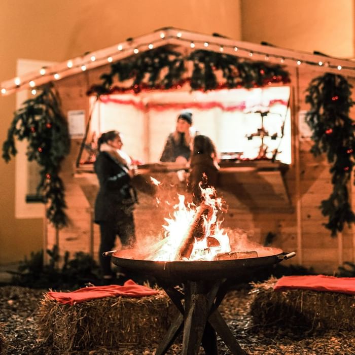 Persone intorno a un falò davanti a una capanna decorata per Natale.