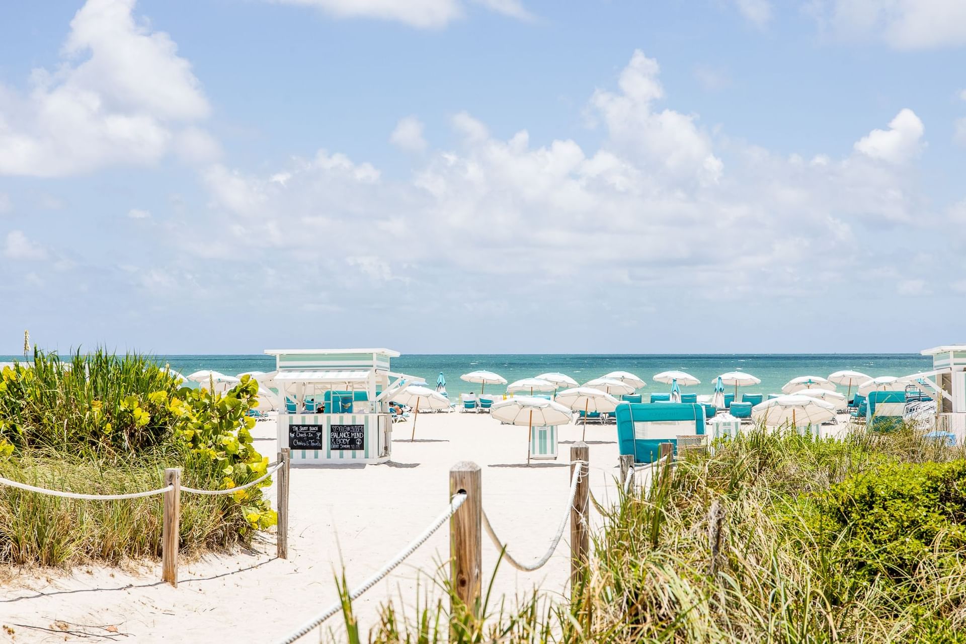 Pathway to a sunny beach lined with sunbeds, umbrellas, and cabanas at The Savoy Hotel & Beach Club