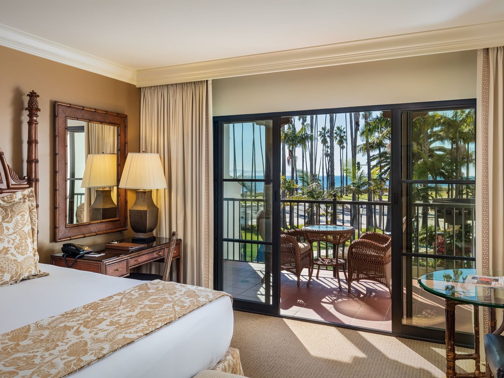 Bright Ocean View One King at Santa Barbara Inn with a chic bed, mirror, and balcony offering ocean views, framed by lawn