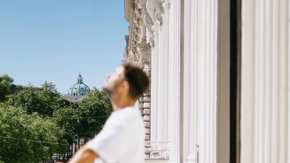 Man standing on a balcony, gazing towards a lush green landscape and a prominent dome structure at Boutique Hotel Vienna