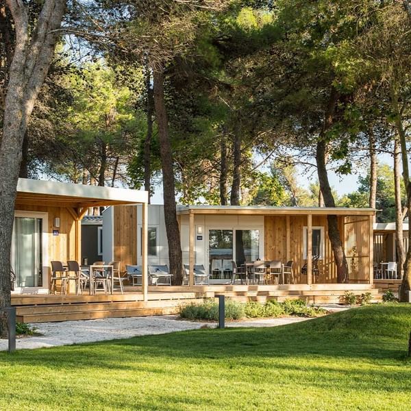 A modern wooden cabin nestled among trees with a furnished outdoor patio at Falkensteiner Premium Camping Zadar