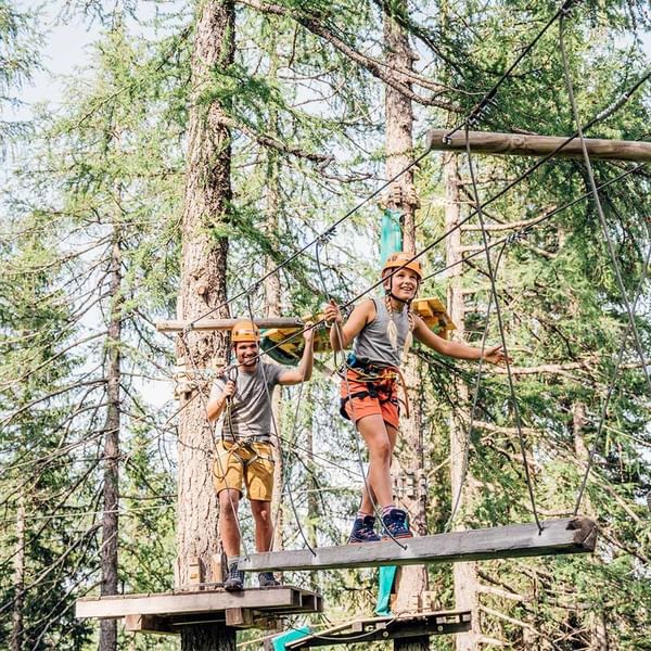 Two people in safety gear on a treetop adventure course near Falkensteiner Hotel & Spa Carinzia